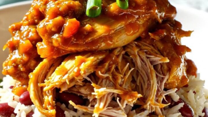 A close-up shot of shredded Jamaican jerk mango chicken served over coconut rice in a bowl, garnished with green scallions.
