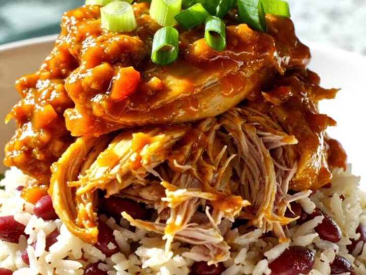 A close-up shot of shredded Jamaican jerk mango chicken served over coconut rice in a bowl, garnished with green scallions.