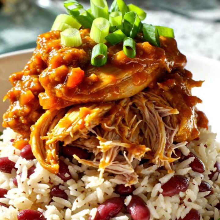 A close-up shot of shredded Jamaican jerk mango chicken served over coconut rice in a bowl, garnished with green scallions.
