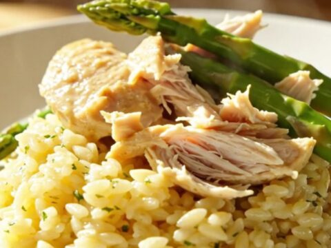 A close-up of creamy lemon mascarpone chicken and tender asparagus in a white ceramic slow cooker.