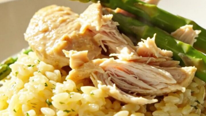 A close-up of creamy lemon mascarpone chicken and tender asparagus in a white ceramic slow cooker.