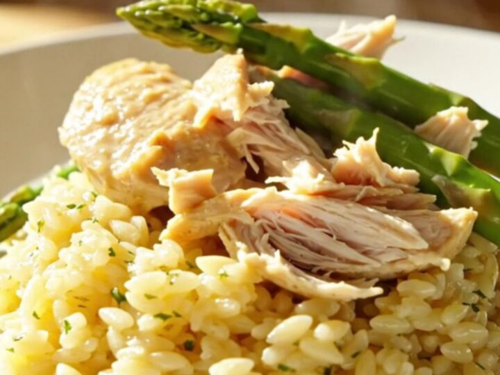 A close-up of creamy lemon mascarpone chicken and tender asparagus in a white ceramic slow cooker.