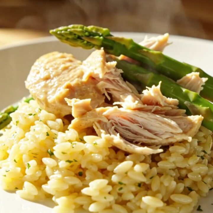 A close-up of creamy lemon mascarpone chicken and tender asparagus in a white ceramic slow cooker.