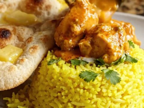 A steaming bowl of creamy chicken tikka masala topped with fresh cilantro, served with rice and naan.