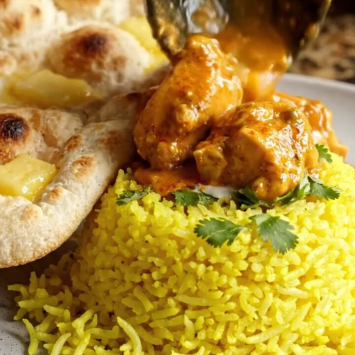 A steaming bowl of creamy chicken tikka masala topped with fresh cilantro, served with rice and naan.