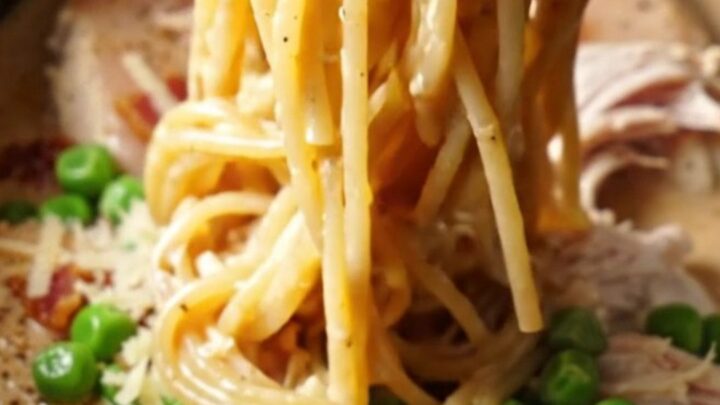 A steaming Crockpot filled with creamy shredded chicken and carbonara sauce.