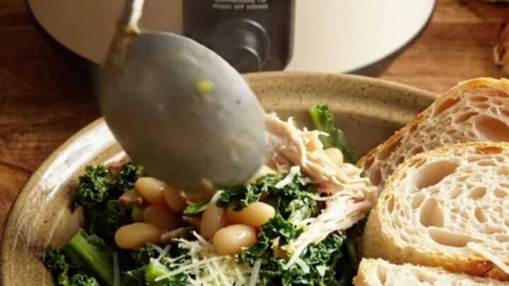 A close-up of creamy Tuscan chicken with kale and white beans in a ceramic slow cooker.