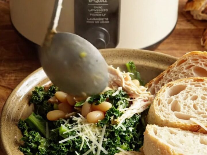 A close-up of creamy Tuscan chicken with kale and white beans in a ceramic slow cooker.