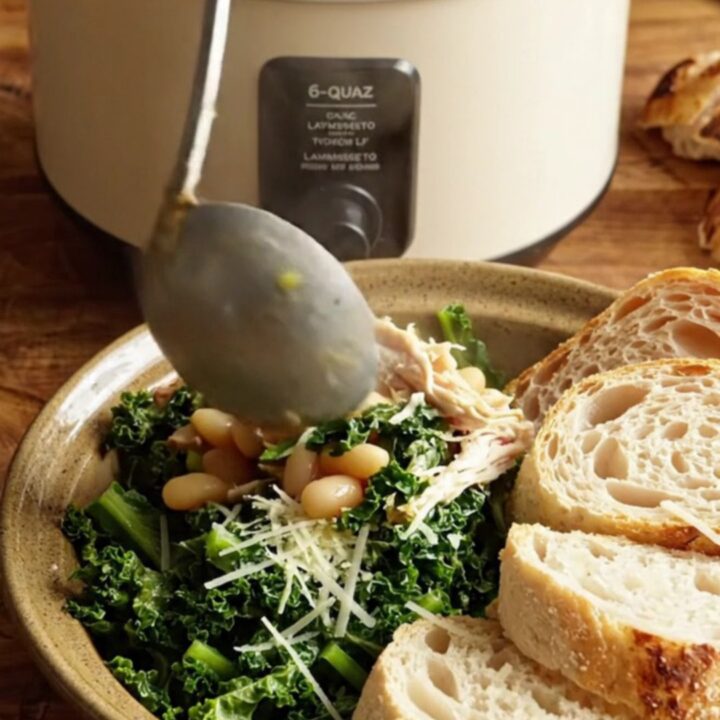 A close-up of creamy Tuscan chicken with kale and white beans in a ceramic slow cooker.