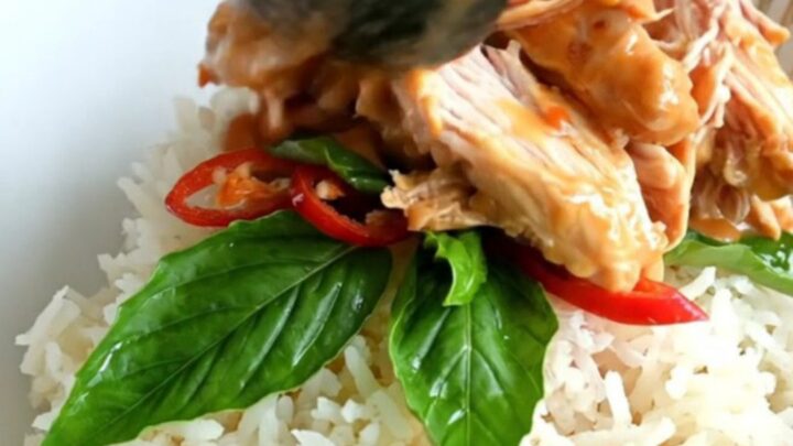 A close-up of shredded chicken in a creamy coconut and sweet chili glaze inside a black ceramic Crockpot.