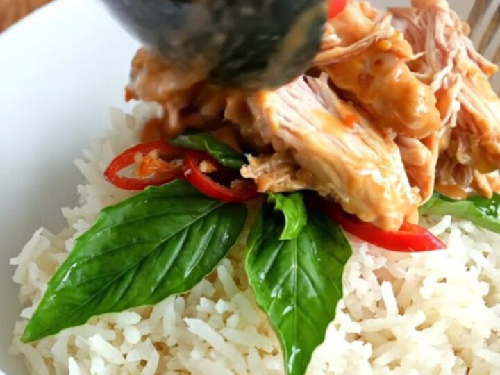 A close-up of shredded chicken in a creamy coconut and sweet chili glaze inside a black ceramic Crockpot.