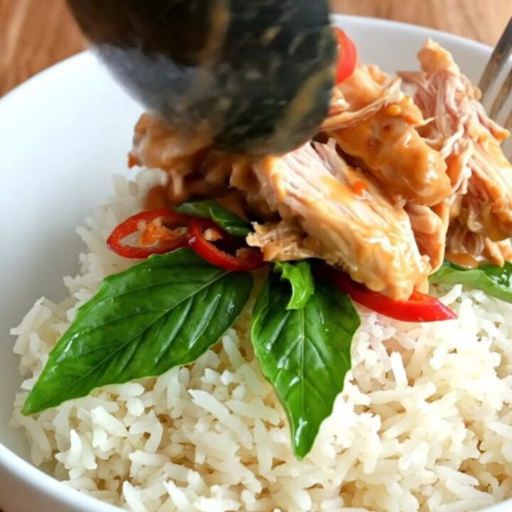 A close-up of shredded chicken in a creamy coconut and sweet chili glaze inside a black ceramic Crockpot.