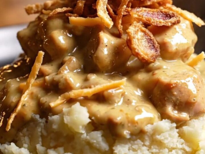 A close-up view of shredded chicken in a creamy, golden sauce with visible melted Gouda and shallots.