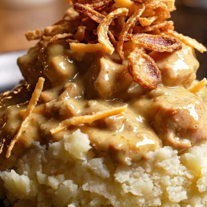 A close-up view of shredded chicken in a creamy, golden sauce with visible melted Gouda and shallots.