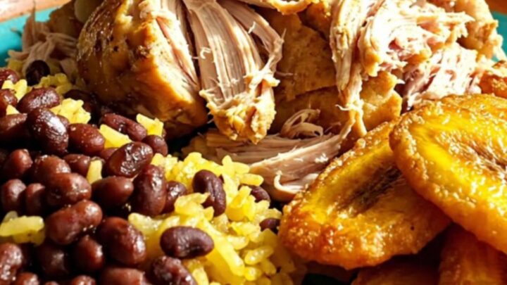 A close-up of tender Cuban Mojo pulled chicken served with yellow rice and beans.