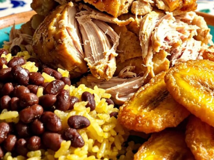 A close-up of tender Cuban Mojo pulled chicken served with yellow rice and beans.