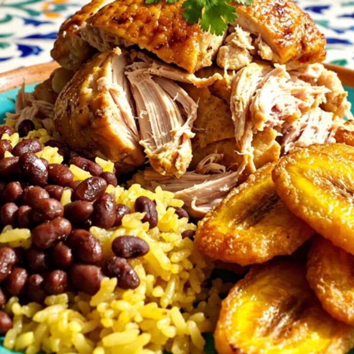 A close-up of tender Cuban Mojo pulled chicken served with yellow rice and beans.