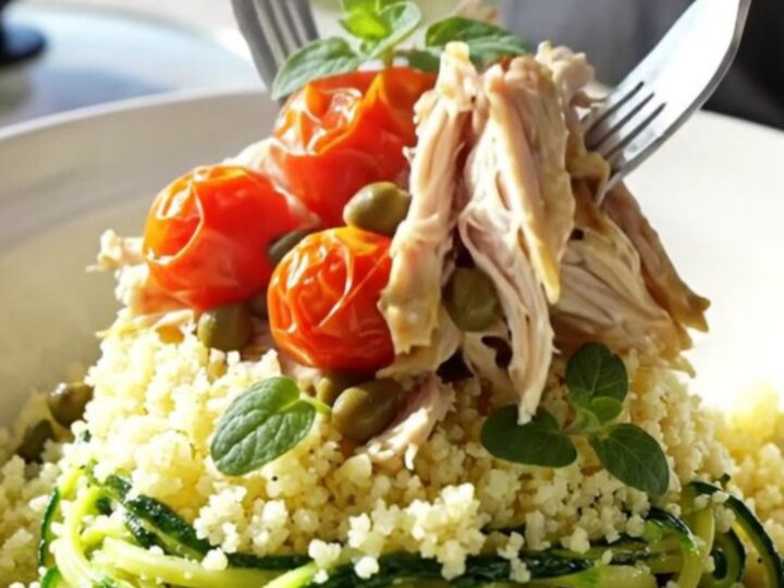 A close-up of tender shredded chicken with artichoke hearts and cherry tomatoes in a light wine sauce.