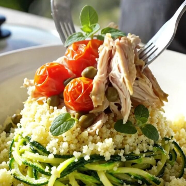 A close-up of tender shredded chicken with artichoke hearts and cherry tomatoes in a light wine sauce.