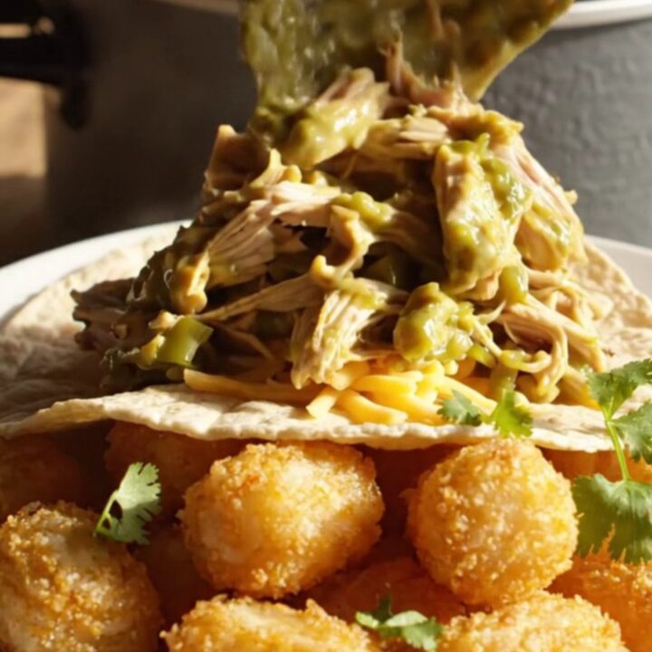 Close up of shredded chicken in a creamy green chile sauce inside a slate ceramic slow cooker.