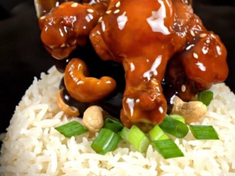 A close-up of glossy Kung Pao chicken with roasted cashews and scallions served in a bowl.