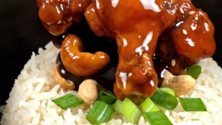 A close-up of glossy Kung Pao chicken with roasted cashews and scallions served in a bowl.