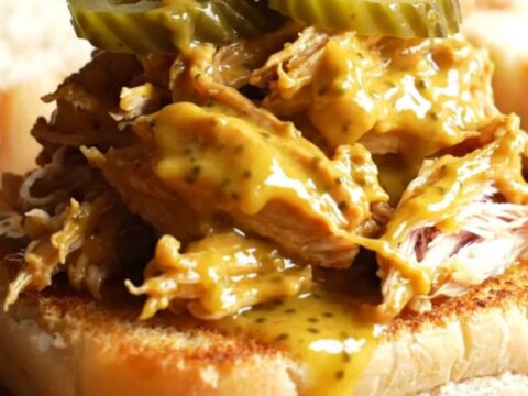 A close-up of shredded Carolina mustard BBQ chicken piled high on a toasted potato roll with slaw.