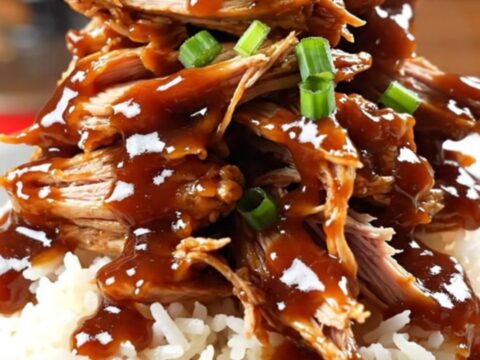 A close-up of Coca-Cola BBQ chicken being shredded with two forks inside a glossy red slow cooker.