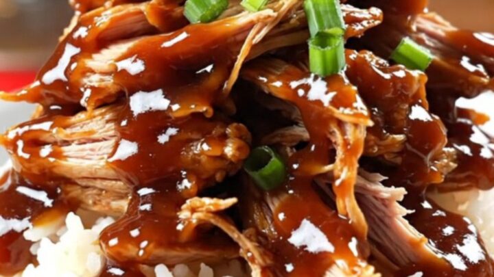 A close-up of Coca-Cola BBQ chicken being shredded with two forks inside a glossy red slow cooker.