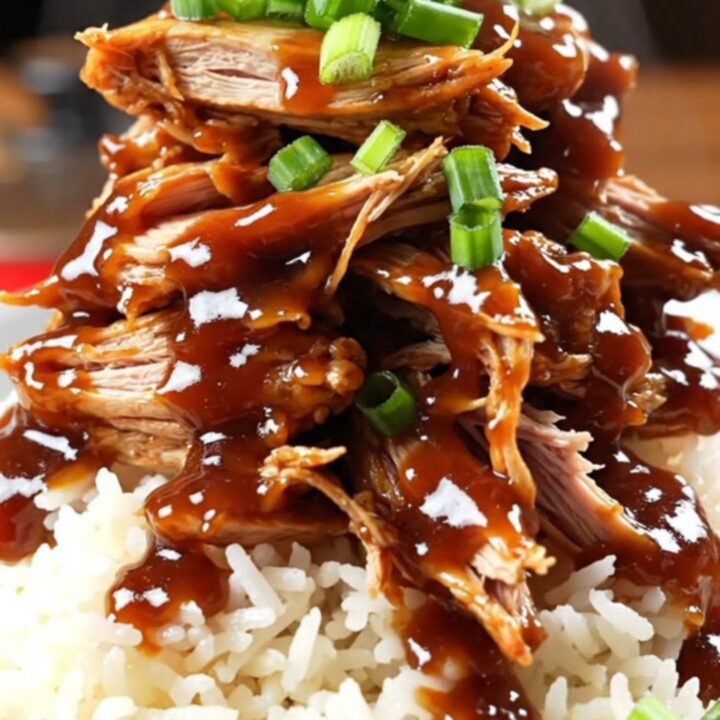 A close-up of Coca-Cola BBQ chicken being shredded with two forks inside a glossy red slow cooker.