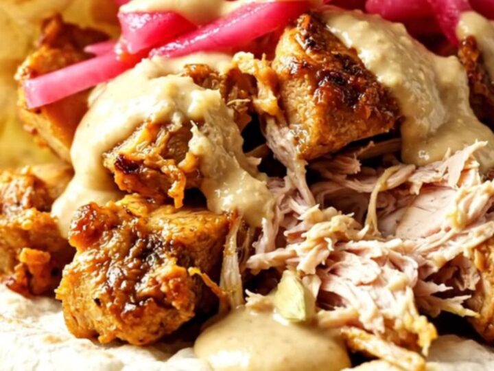 Close-up of shredded chicken shawarma being pulled from a slow cooker with two forks.