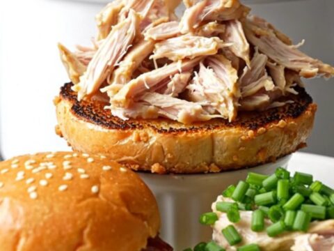 A ceramic slow cooker filled with creamy, shredded everything bagel crack chicken topped with fresh chives.