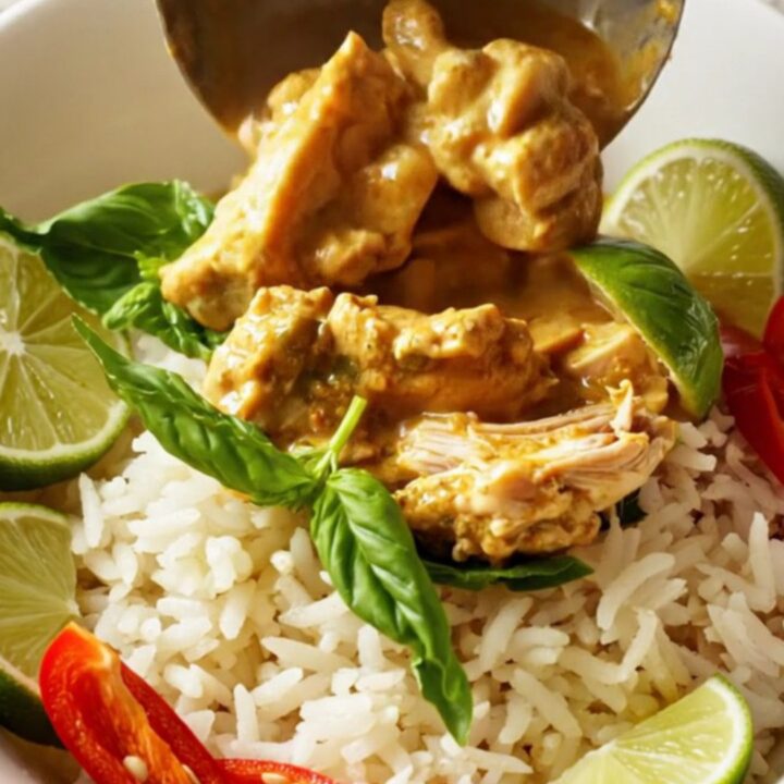 A steaming bowl of coconut red curry chicken served over jasmine rice with fresh basil and lime wedges.