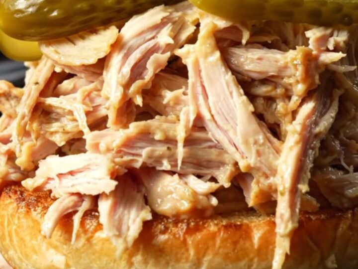 A close-up of a succulent Alabama white BBQ pulled chicken sandwich on a toasted brioche bun with a pickle spear.