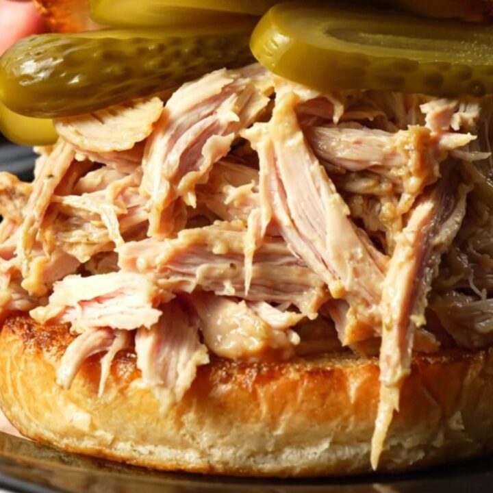 A close-up of a succulent Alabama white BBQ pulled chicken sandwich on a toasted brioche bun with a pickle spear.