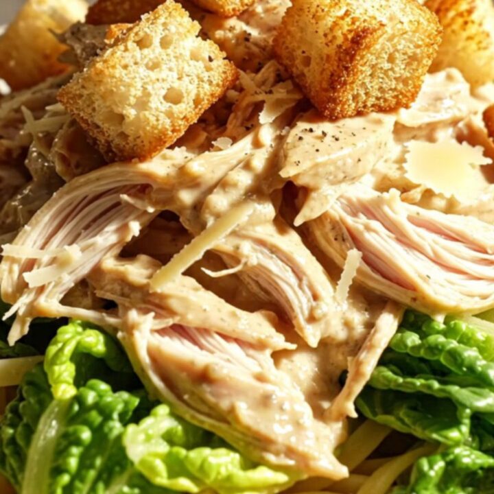 A close-up of creamy Caesar shredded chicken in a white ceramic slow cooker with parmesan and pepper.