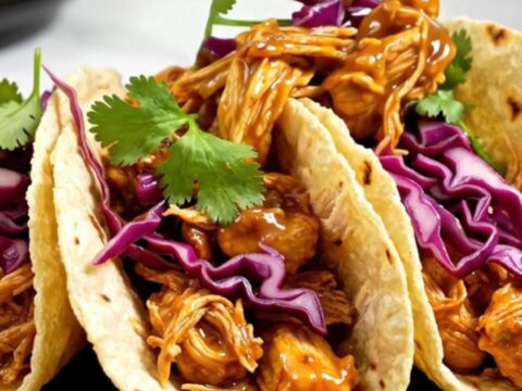 A close-up of slow-cooked pulled chicken in a glossy mango habanero glaze served in a street taco with cabbage and cilantro.
