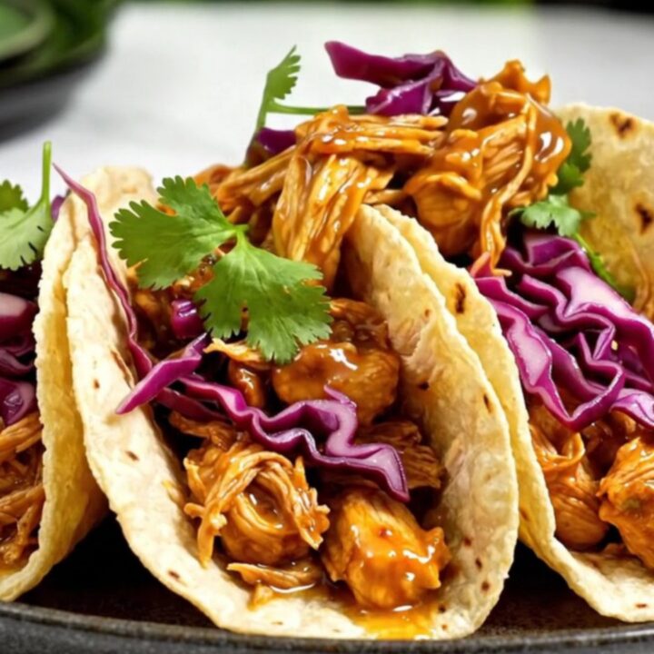 A close-up of slow-cooked pulled chicken in a glossy mango habanero glaze served in a street taco with cabbage and cilantro.