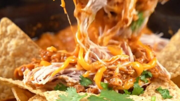 A warm red slow cooker filled with creamy shredded chicken, chorizo, and melted white queso, topped with cilantro.