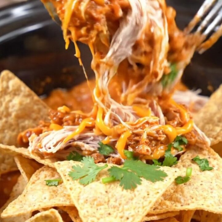 A warm red slow cooker filled with creamy shredded chicken, chorizo, and melted white queso, topped with cilantro.
