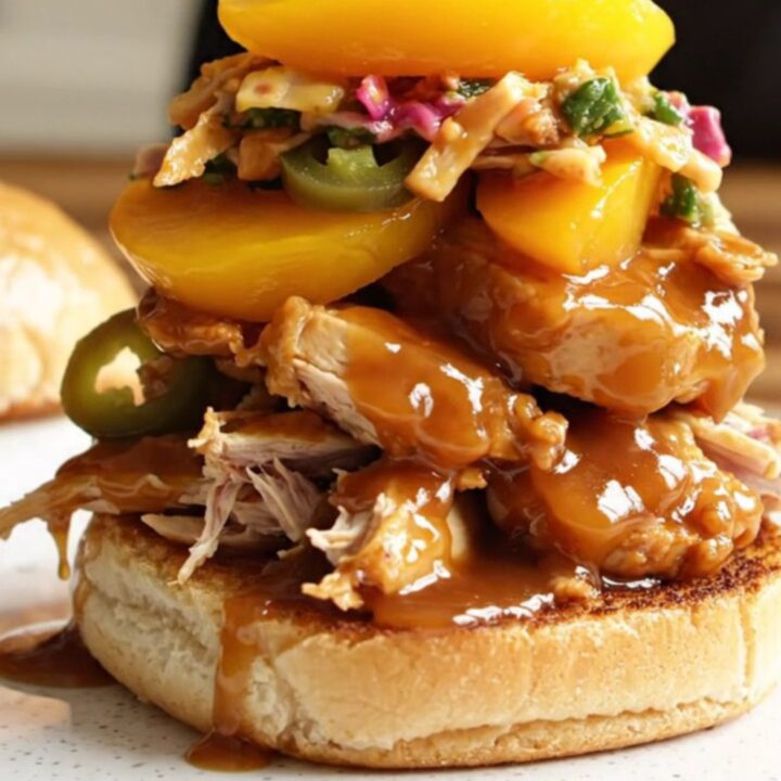 A close-up of succulent pulled chicken in a rich, amber-colored peach bourbon glaze piled high on a toasted brioche bun.