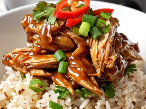A close-up of tender, shredded Vietnamese caramel chicken in a black ceramic slow cooker
