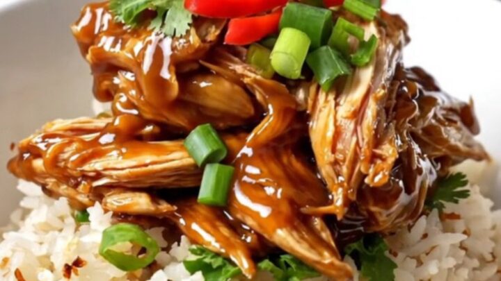 A close-up of tender, shredded Vietnamese caramel chicken in a black ceramic slow cooker