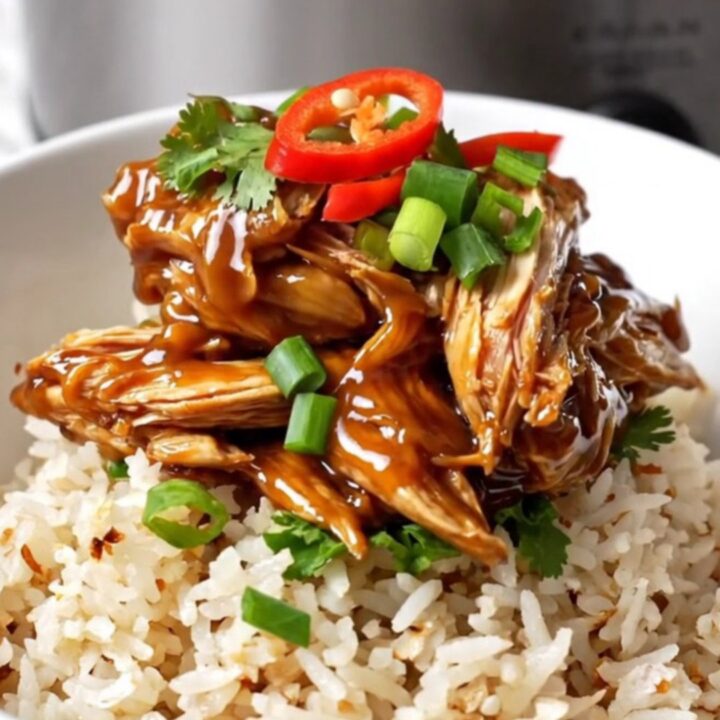 A close-up of tender, shredded Vietnamese caramel chicken in a black ceramic slow cooker