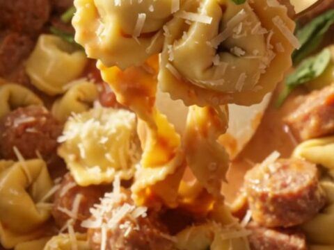 A steaming bowl of creamy sausage and tortellini pasta topped with fresh basil and grated Parmesan cheese.