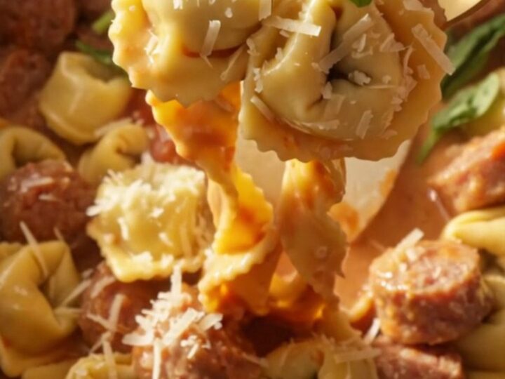 A steaming bowl of creamy sausage and tortellini pasta topped with fresh basil and grated Parmesan cheese.