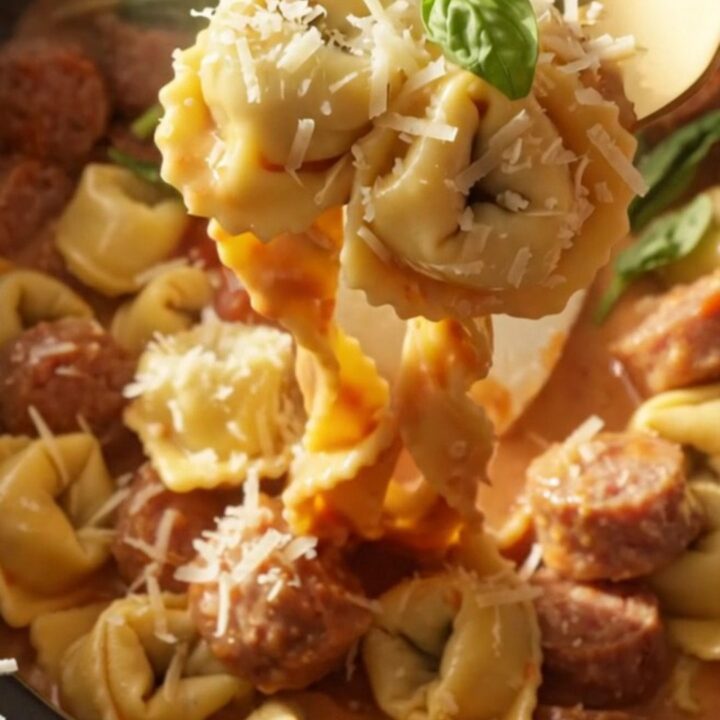 A steaming bowl of creamy sausage and tortellini pasta topped with fresh basil and grated Parmesan cheese.