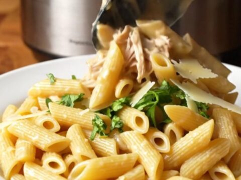 A close-up of creamy garlic parmesan chicken pasta in a slow cooker with visible shredded chicken and melted cheese.
