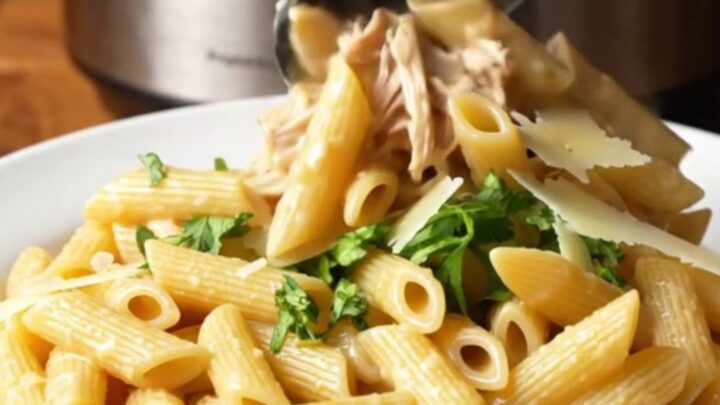 A close-up of creamy garlic parmesan chicken pasta in a slow cooker with visible shredded chicken and melted cheese.