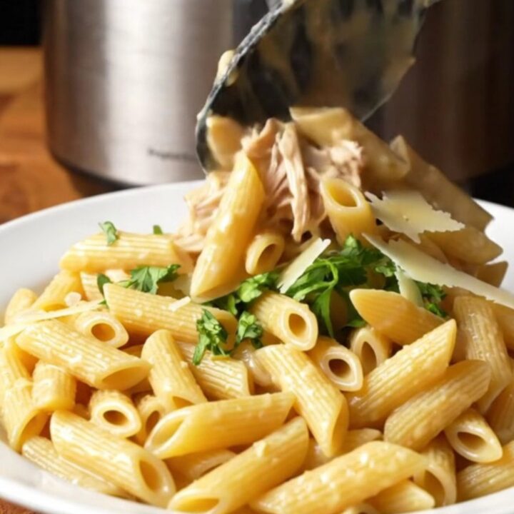 A close-up of creamy garlic parmesan chicken pasta in a slow cooker with visible shredded chicken and melted cheese.